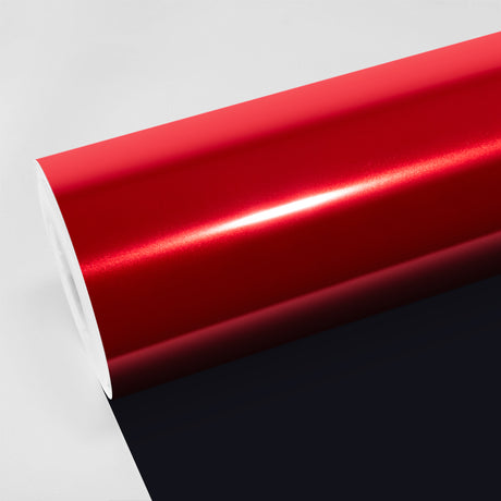 Glossy chrome-like Inferno Red vinyl wrap roll (CHM24-HD) from TeckWrap, shown partially unrolled on a white and black surface, reflecting bright light across its mirror-red finish.